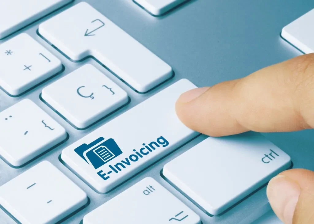 Dłoń naciskająca klawisz E-Invoicing na klawiaturze, symbolizująca automatyzację obiegu dokumentów w firmie za pomocą AI.