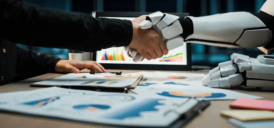 Uścisk dłoni człowieka i robota nad wykresami biznesowymi, ilustrujący synergię technologii AI z procesami w firmie.