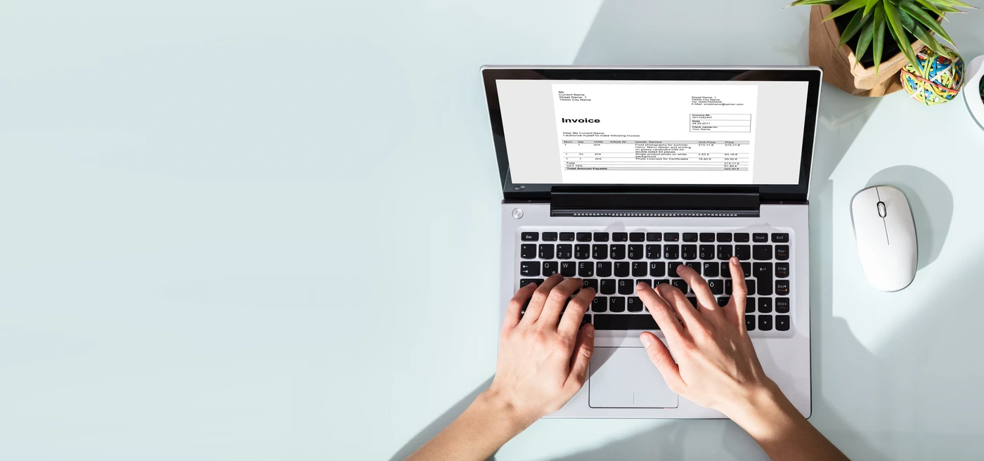 Widok z góry na dłonie pracownika obsługującego cyfrową fakturę na laptopie podczas wdrożenia systemu KSeF w firmie.