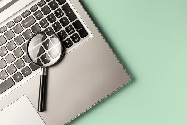 Lupa na klawiaturze laptopa jako symbol szczegółowej analizy i profesjonalnego audytu infrastruktury IT.