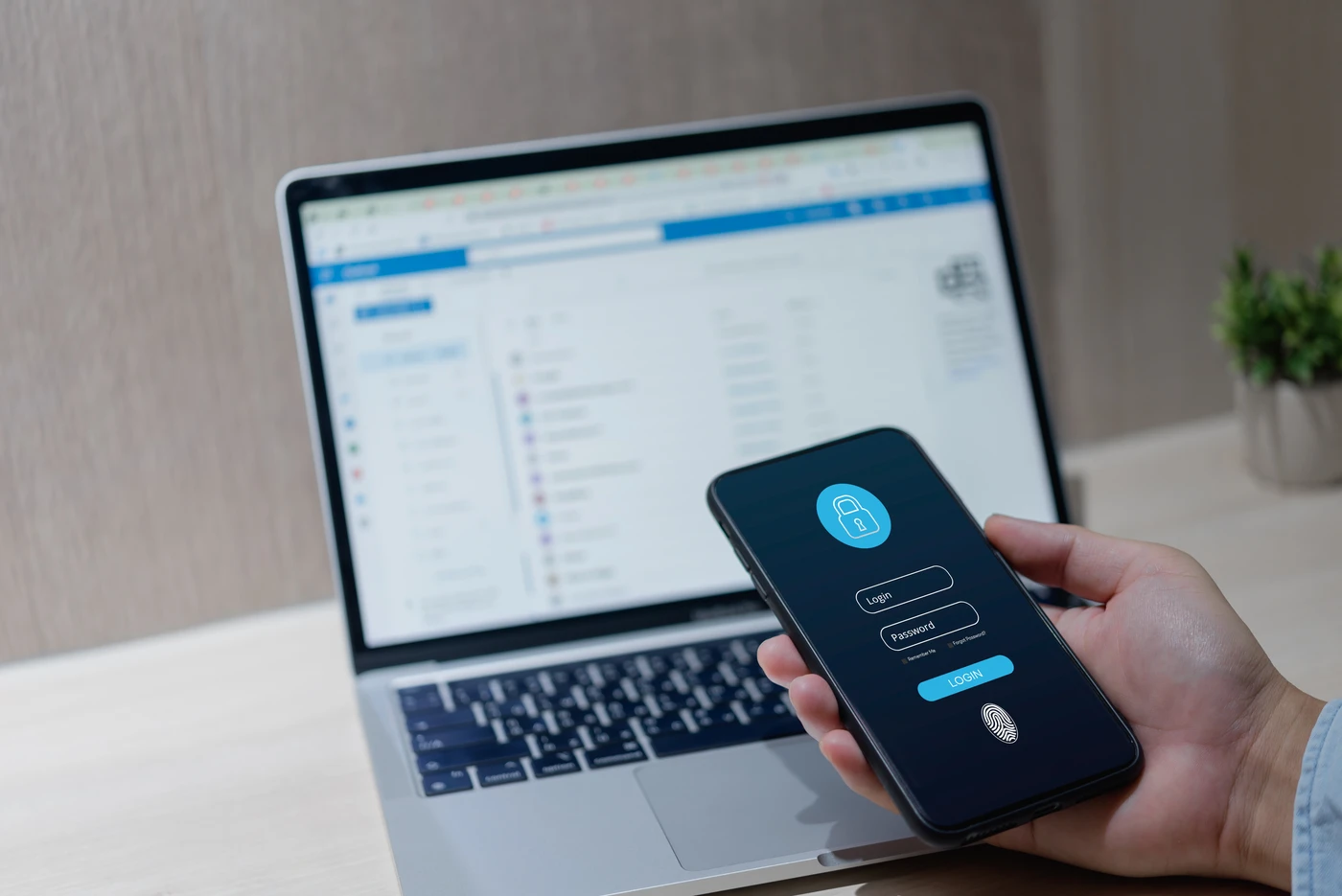 Smartfon z ekranem logowania i ikoną odcisku palca obok laptopa – przykład wdrożenia dwuetapowej autentykacji (MFA) w firmie.