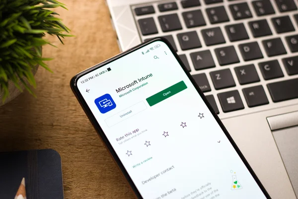Smartfon z otwartym sklepem aplikacji i widocznym panelem instalacji Microsoft Intune na drewnianym biurku.