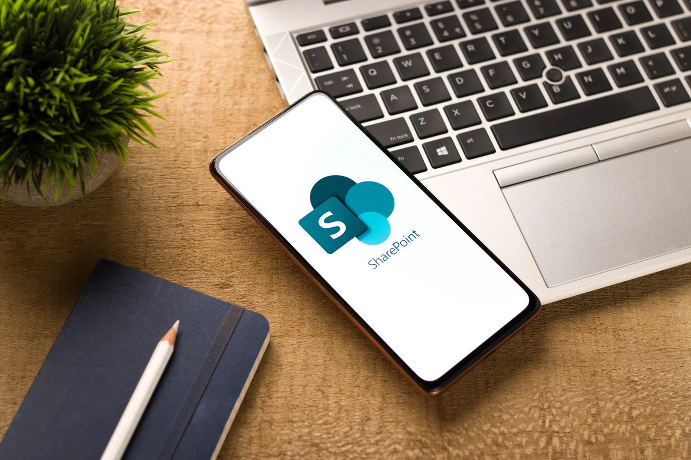 Smartfon wyświetlający logo SharePoint obok laptopa, prezentujący mobilny dostęp do plików w ramach usług Microsoft 365.