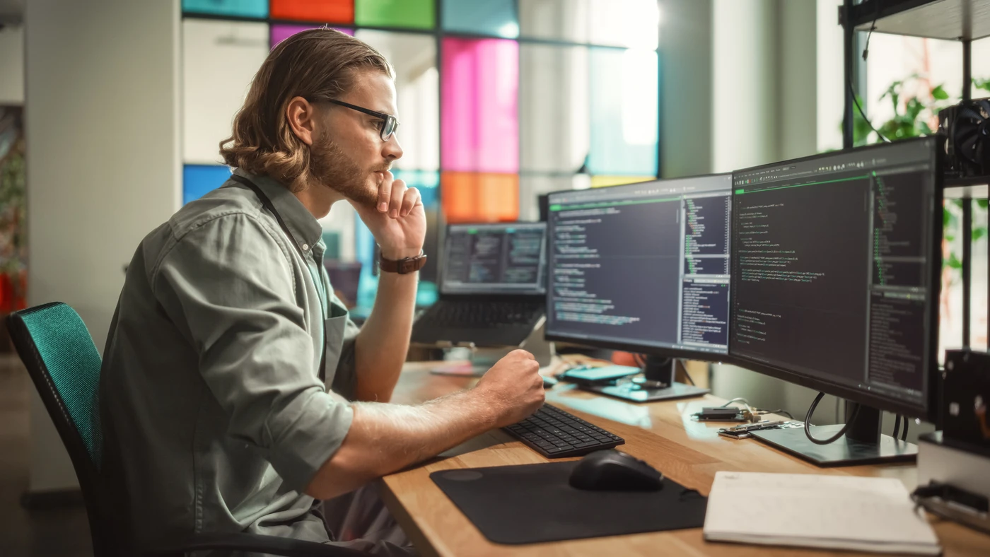 Programista pracujący przy kilku monitorach nad kodem – profesjonalna obsługa informatyczna dla firm.