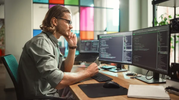 Programista pracujący przy kilku monitorach nad kodem – profesjonalna obsługa informatyczna dla firm.