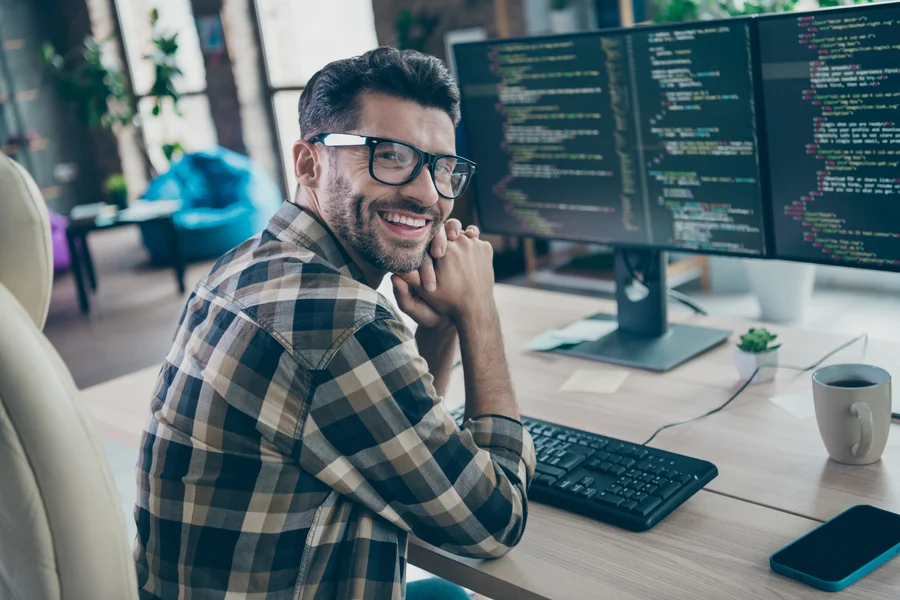 Uśmiechnięty programista eBimedia przy stanowisku z kodem źródłowym, zapewniający stabilne działanie monitoringu Zabbix.