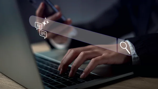 Dłonie użytkownika na klawiaturze laptopa z nałożoną grafiką inteligentnego paska wyszukiwania AI i ikonami czatu.
