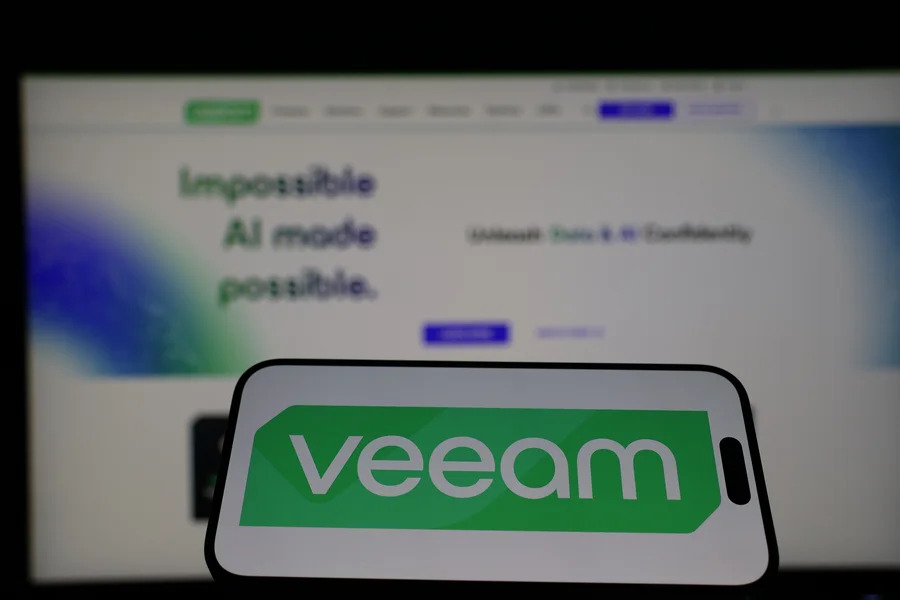 Smartfon z logo Veeam na tle ekranu komputera – profesjonalne rozwiązania do backupu i przywracania danych dla firm.